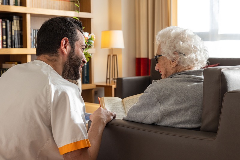 trabajdor de la residencia ayudando a leer a una anciana